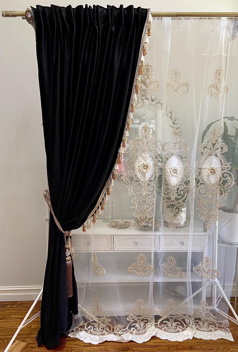 Pu&ograve; includere: Elegante tenda in velluto nero abbinata a una tenda bianca trasparente con ricami dorati ornati. Le tende sono decorate con nappe decorative e sono progettate per uno stile di arredamento sofisticato.