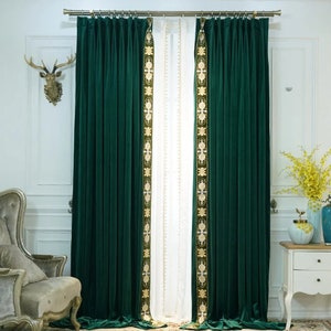 May include: Dark green velvet curtains with gold embroidered detailing. The curtains are suspended from a gold rail and frame a white sheer curtain. The room has a classic, elegant style.