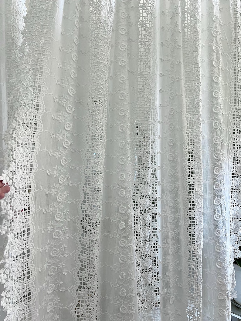 May include: White lace curtain with floral and geometric patterns. The curtain features intricate details, including roses and openwork designs. The fabric appears to be delicate and airy, creating a soft, romantic aesthetic.