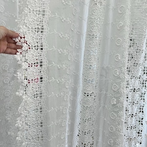May include: White lace curtain with floral and geometric patterns. The curtain features intricate embroidered details, including flowers and openwork designs. The delicate fabric is semi-sheer, allowing light to filter through.