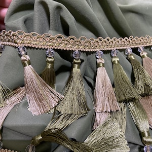 May include: Olive green fabric with decorative trim featuring gold and beige tassels. The trim has a gold and beige scalloped edge with clear, faceted beads. The tassels are in shades of gold and olive green.