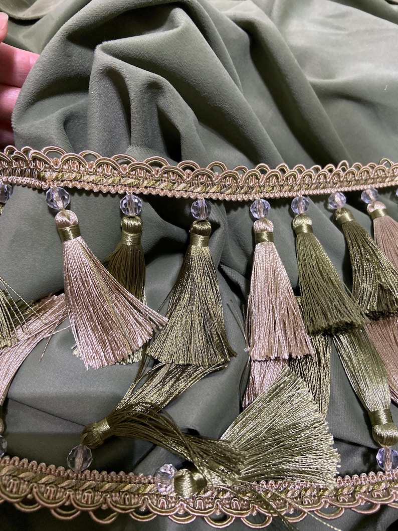 May include: Olive green fabric with decorative trim featuring gold and beige tassels. The trim has a gold and beige scalloped edge with clear, faceted beads. The tassels are in shades of gold and olive green.