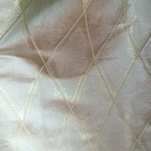 May include: Close-up of a fabric with a diamond pattern. The fabric has a pearlescent sheen with a light beige and white color scheme. The diamond pattern is created by thin, light gold lines.