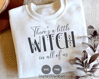 Puede incluir: Sudadera blanca con el texto "There's a little witch in all of us" en letras negras. El texto está decorado con estrellas y formas geométricas. La sudadera está doblada y se muestra sobre una superficie con estampado.