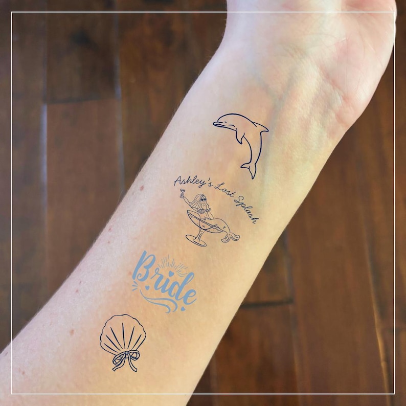 May include: Temporary tattoos in blue ink, featuring a dolphin, a mermaid with a cocktail, a seashell, and the word "Bride". The phrase "Ashley's Last Splash" is also included. These temporary tattoos are perfect for a bachelorette party or bridal shower.
