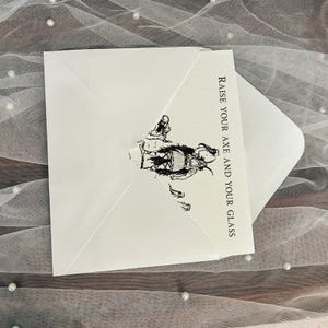 以下が含まれることがあります： 白の封筒と、戦士の白黒イラストと「Raise your axe and your glass」の文字が入ったカード。封筒は開いており、中のカードが見えています。