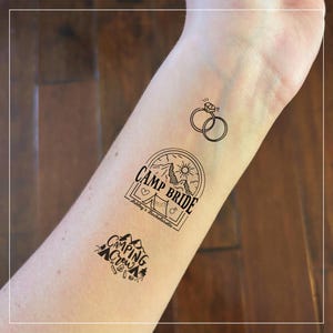 May include: Black temporary tattoos featuring a wedding ring design, a "Camp Bride" badge with a tent and mountain scene, and a "Camping Crew" badge with mountains and camping gear. Perfect for a bachelorette party or camping themed event.