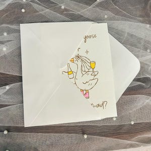 May include: White greeting card with a cartoon goose illustration holding a champagne bottle and a glass of wine. The text "goose maid?" is handwritten on the card. The card is inside a white envelope.