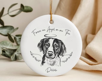 Puede incluir: Adorno navideño redondo de cerámica blanca con cordón dorado. Presenta una ilustración de perro en blanco y negro con alas de ángel y un halo. El texto dice "Forever an Angel on our Tree" y el nombre "Delilah".