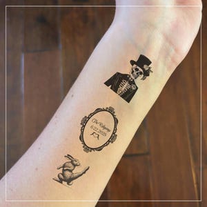 May include: Three temporary tattoos on a person's arm. The tattoos are black and white and feature a skeleton in a top hat, a rabbit, and a framed design with the text "The Ridgeways 6.22.2025".