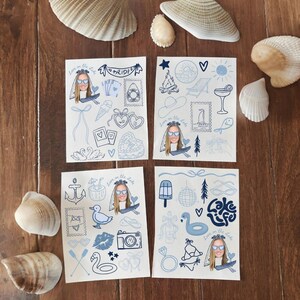 May include: Four white cards with blue illustrations and text, including a bride with sunglasses, hearts, and lake-themed icons. Seashells surround the cards on a wooden surface. The text "Love on the Lake" and "Lake Life" are visible.