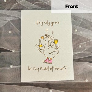 May include: A white card with the text "Hey silly goose" and "be my maid of honor?" features a cartoon goose holding a bottle and a glass of wine. The goose wears pink shoes and a headpiece.