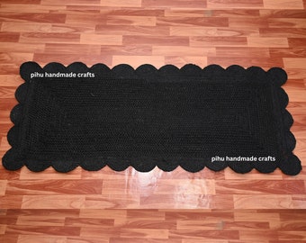 May include: Black jute rug with a scalloped edge. The rug is handmade and has the text "pihu handmade crafts" on it.