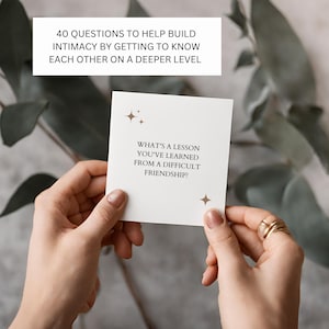 May include: A white card with gold stars and the text "What's a lesson you've learned from a difficult friendship?"  The card is being held by a person's hands.
