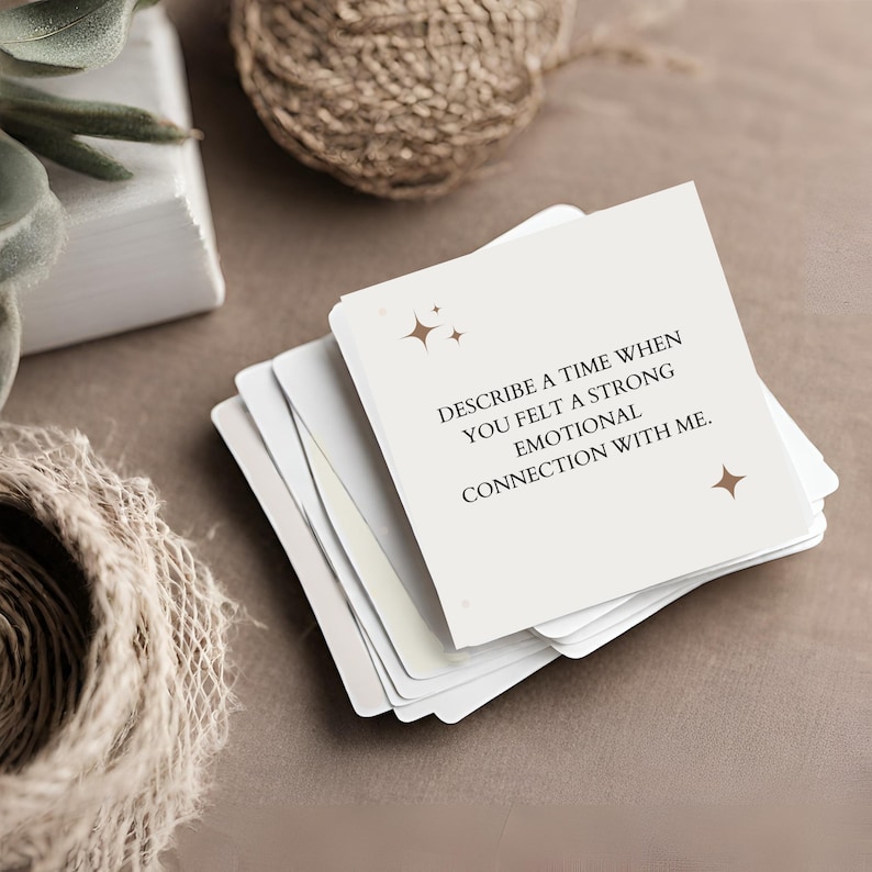 May include: A stack of white cards with a brown background. The top card has the text "Describe a time when you felt a strong emotional connection with me." with two gold stars on either side of the text.