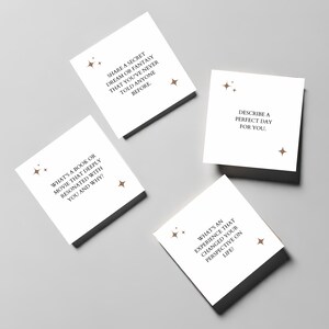 May include: Four white cards with brown text and star-shaped designs. The cards contain prompts for conversation starters, such as "What's a book or movie that deeply resonated with you and why?" and "Share a secret dream or fantasy that you've never told anyone before."