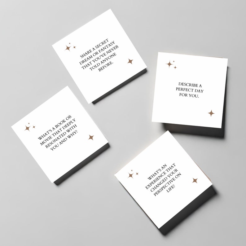 May include: Four white cards with brown text and star-shaped designs. The cards contain prompts for conversation starters, such as "What's a book or movie that deeply resonated with you and why?" and "Share a secret dream or fantasy that you've never told anyone before."