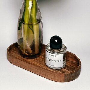 A clear vase with white and pink flowers on an oval wooden tray, beside a small jar labeled "BYREDO GYPSY WATER."