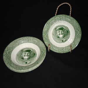 Puede incluir: Juego de cuatro cuencos de cerámica verde y blanco con un diseño vintage que presenta a un hombre con un sombrero y una pipa. Los cuencos están apilados uno encima del otro y tienen un borde decorativo.