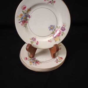 May include: Set of four white floral dessert plates with a gold rim. The plates feature a delicate floral pattern in shades of pink, yellow, and blue.