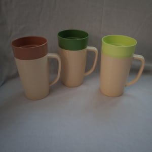 May include: Three tall mugs with ribbed, cream-colored bodies and handles. Each mug features a distinctively colored rim: one in muted brown, one in forest green, and one in lime green. The mugs have a cylindrical shape and a smooth, uniform texture.