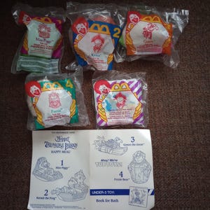May include: Five sealed McDonald's Muppet Treasure Island tub toys in plastic packaging, including Miss Piggy, Kermit, Gonzo, Fozzie, and a bath book, accompanied by a white paper toy reference card featuring character illustrations and instructions.