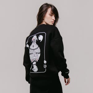May include: Black sweatshirt with a white graphic of a playing card featuring a character with a crown and a sword. The card has the number nine and quotation marks on it.