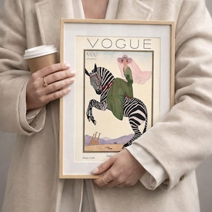 Digitally restored 1926 Vogue magazine cover titled Southern Fashions Number, featuring a stylish woman in a flowing green dress and pink hat riding a zebra in a desert landscape with giraffes and mountains. Vintage Art Deco fashion illustration digital download ideal for gallery walls, eclectic decor, and gifts for fashion history and vintage art lovers.