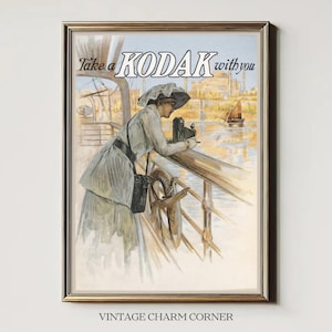 May include: Vintage framed print featuring a woman using a Kodak camera on a boat deck. The image has a sepia tone with the text "Take a Kodak with you" at the top. The print is in a gold frame and has the text "VINTAGE CHARM CORNER" at the bottom.