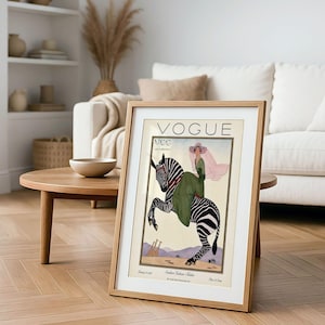 Digitally restored 1926 Vogue magazine cover titled Southern Fashions Number, featuring a stylish woman in a flowing green dress and pink hat riding a zebra in a desert landscape with giraffes and mountains. Vintage Art Deco fashion illustration digital download ideal for gallery walls, eclectic decor, and gifts for fashion history and vintage art lovers.