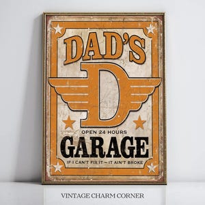 May include: A vintage-style sign with a distressed orange background and black text. The sign reads "Dad's Garage Open 24 Hours If I Can't Fix It - It Ain't Broke". The sign features a large orange letter "D" with wings and stars.