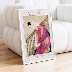 May include: Framed Vogue magazine cover art print. The vintage illustration depicts a woman in a white dress with a long, feathered train descending a staircase. The print has a white border and the Vogue logo at the top.