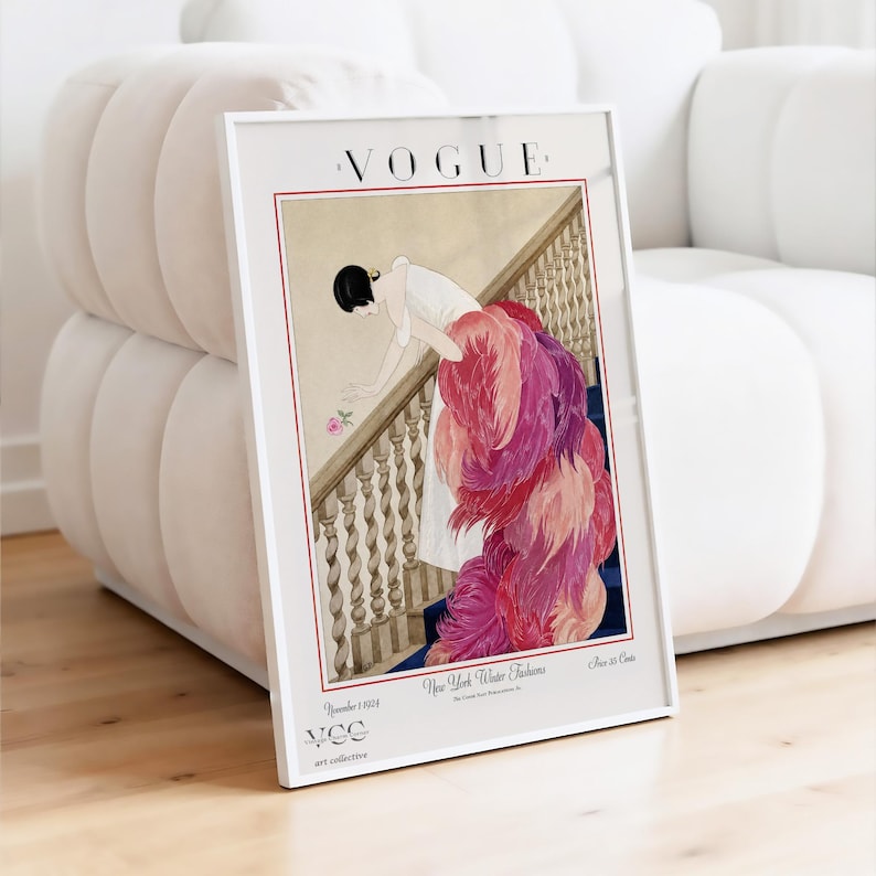 May include: Framed Vogue magazine cover art print. The vintage illustration depicts a woman in a white dress with a long, feathered train descending a staircase. The print has a white border and the Vogue logo at the top.
