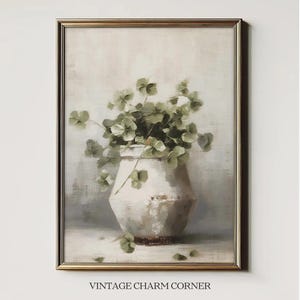 Może przedstawiać: Biały ceramiczny wazon o rustykalnym wykończeniu wypełniony zielonymi liśćmi koniczyny na jasnoszarym tle.