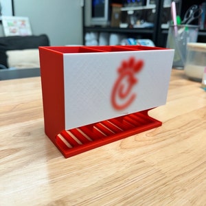 May include: Red and white plastic desk organizer with three compartments. The front of the organizer has the Chick-fil-A logo.