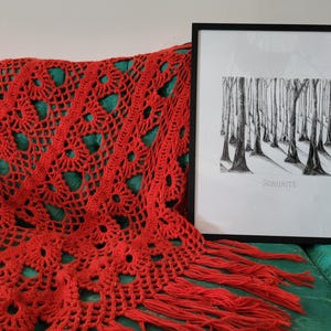 May include: A black and white drawing of a forest with the word "SORORITE" printed below. The drawing is framed and hanging on a wall above a red crocheted throw blanket.