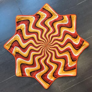 Puede incluir: Una alfombra de suelo en forma de estrella con un diseño de remolino naranja, rojo y amarillo.