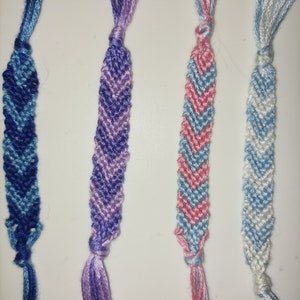 May include: Four friendship bracelets with chevron patterns in blue, purple, pink, and white.