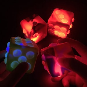 Puede incluir: Cuatro dados luminosos de colores con diferentes patrones. Los dados están hechos de un material suave y esponjoso y brillan en la oscuridad.