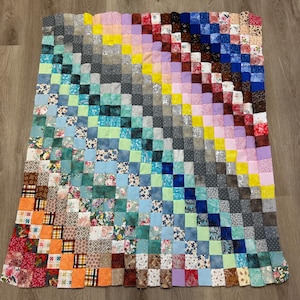 May include: A colourful patchwork quilt, hand-stitched from numerous small, square fabric pieces. The quilt displays a variety of patterns and colours, including blue, green, yellow, pink, and orange. The design creates a visually interesting and textured surface, suitable for a bed or sofa.