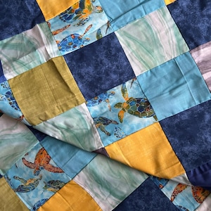 May include: A patchwork quilt with a blue, yellow, and green color scheme. The quilt features a repeating pattern of sea turtles in a variety of poses.