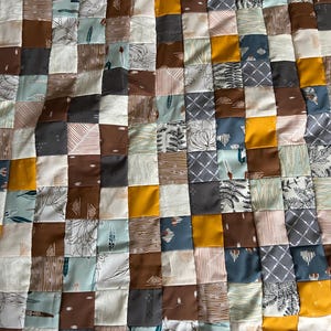 Può includere: Una trapunta patchwork con una varietà di motivi e colori, tra cui marrone, giallo, grigio e blu. La trapunta è composta da quadrati di tessuti diversi, ognuno con un design unico.
