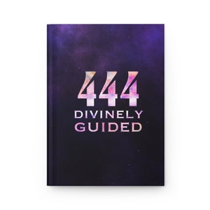 May include: A black notebook with a galaxy-like design and the number 444 in pink and white. The text "DIVINELY GUIDED" is printed below the number.