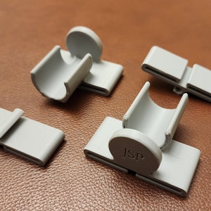 May include: Four gray plastic clips, two with a circular base and a hollow tube, and two flat clips with a split in the middle. One of the circular clips has the letters "JSP" printed on the base.