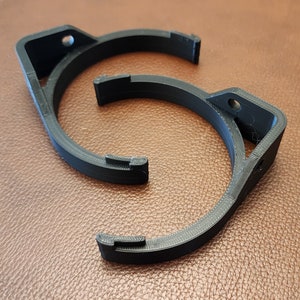 May include: Two black plastic 3D printed brackets with a circular opening. The brackets are designed to be mounted to a wall or other surface.