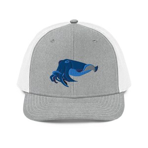 Könnte beinhalten: Graue Trucker-Cap mit weißem Mesh-Rücken und einem blauen, gestickten Tintenfisch-Design auf der Vorderseite. Der Tintenfisch ist mit Blautönen detailliert und hat eine geschwungene Form.