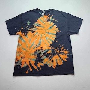Könnte beinhalten: Ein schwarzes T-Shirt mit einem Batik-Muster in Orange- und Blautönen. Das Muster ist ein Wirbeldesign mit einem zentralen Punkt.
