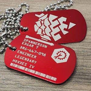 May include: Two red dog tags with silver ball chains. One tag has a white geometric design, the other has text: SPANNERSON EDGAR T, DRG-667-098, ENGINEER, LEGENDARY, HOXXES IV, and a white gear icon.