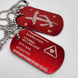 May include: Two red metal dog tags on a silver chain. The top tag has a white symbol, and the bottom tag has the text "DOOMSLAYER", "ETERNAL", "HELLWALKER", "R/T-666", and "12101993".