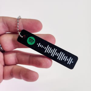 May include: Black keychain with a white Spotify barcode and a green Spotify logo.